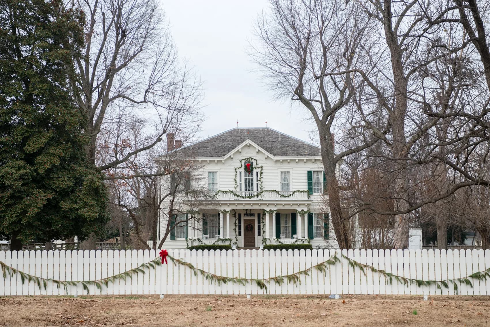 The white Hunter-Dawson house behind a picket fence trimmed with garland